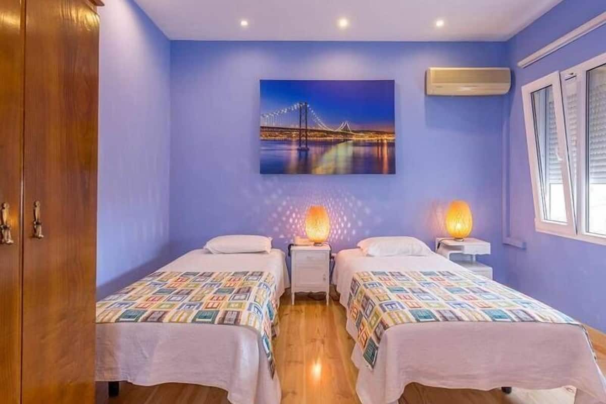 Una habitación con dos camas, un armario de madera, un cuadro de un puente y un equipo de aire acondicionado.
