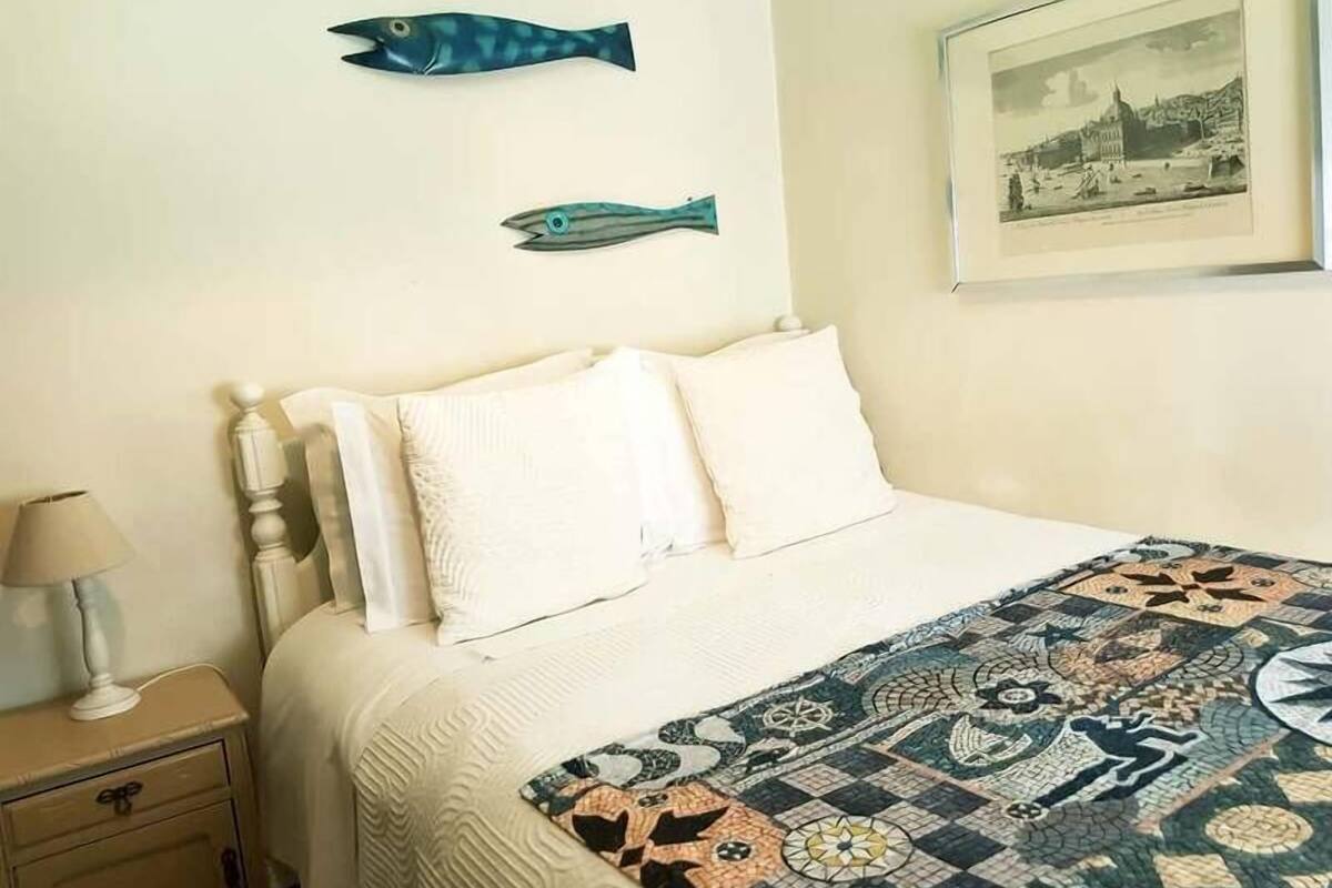 Un dormitorio con cama, almohadas, una mesita de noche, una lámpara y dos adornos en la pared.