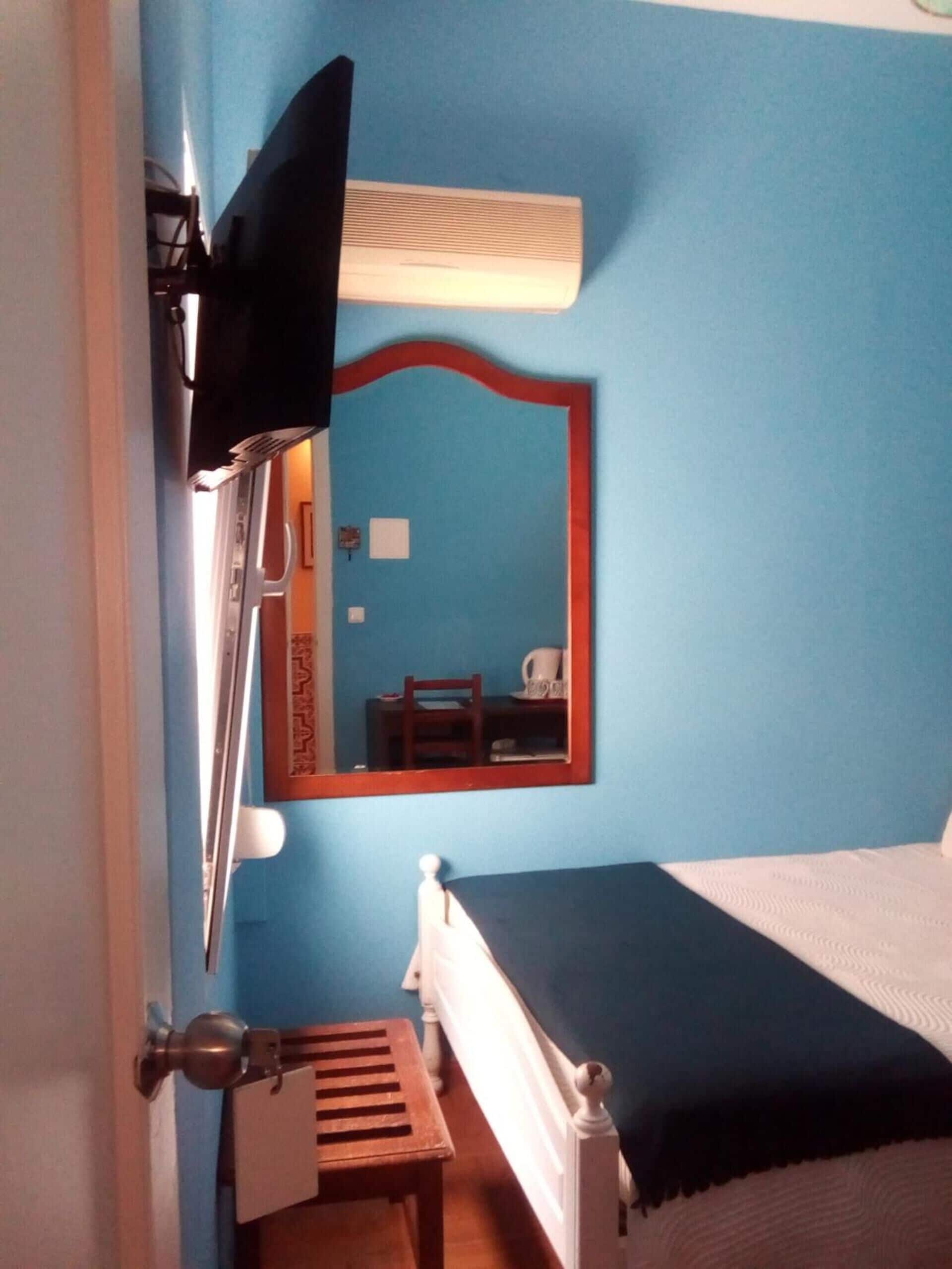 A bedroom with a single bed, a bedside table, a mirror, and a window with blinds.