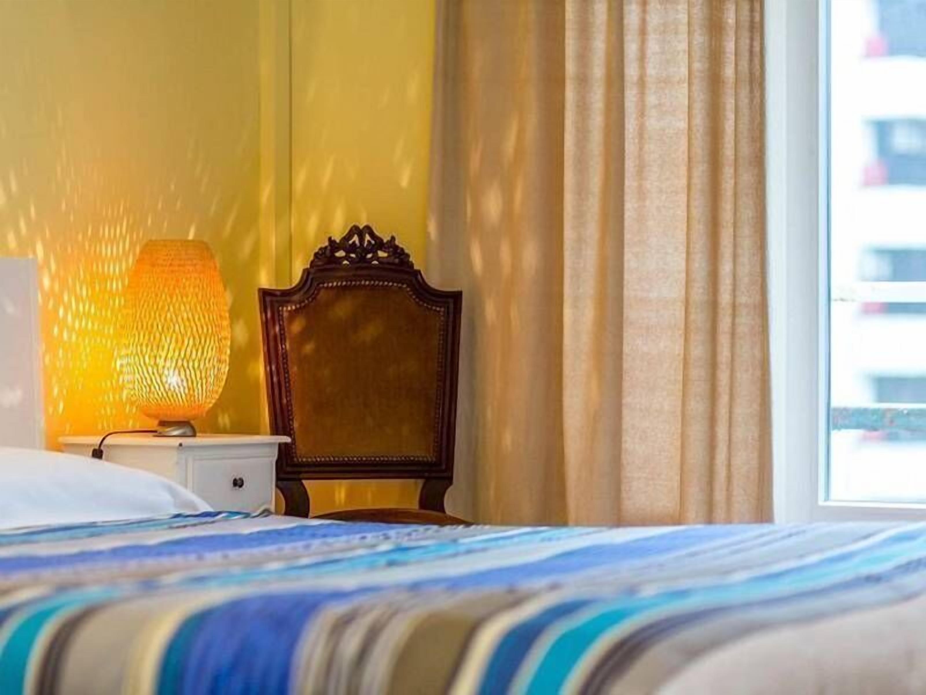 A hotel room with a bed, a nightstand with a lamp, and a chair.