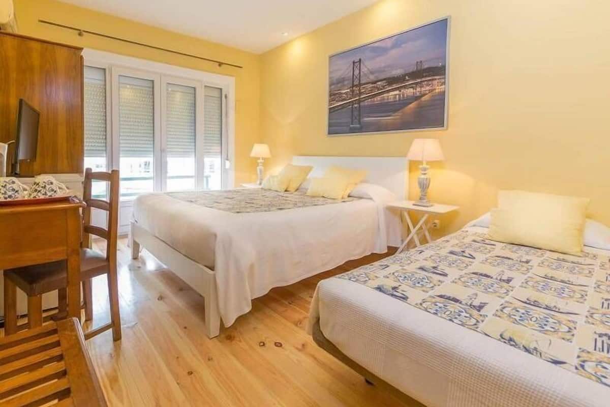 Habitación de hotel con dos camas, un escritorio y una silla. Se observa una ventana con persianas y un cuadro en la pared.