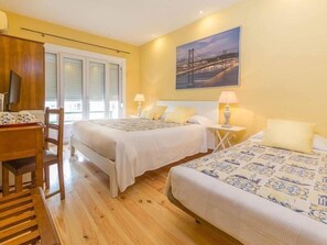 A hotel room with two beds, a desk, and a chair. There is a window with blinds and a painting on the wall. - Casa Belmonte (Lisbon)