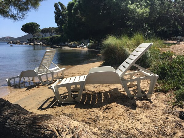 A beach with white lounge chairs and a calm sea.