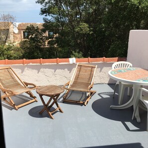 A terrace with two wooden lounge chairs, a small round table, and a white chair.