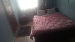 Een slaapkamer met een bed, nachtkastje, raam met gordijnen en een stopcontact.