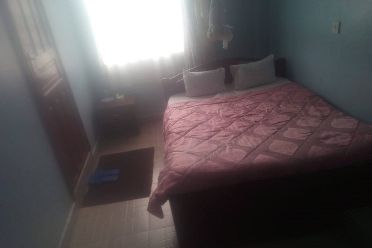 A bedroom with a bed, a nightstand, a window with curtains, and a wall socket.