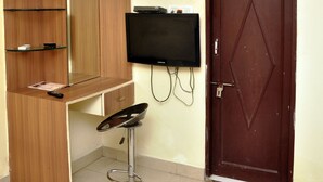 Une pièce avec un meuble en bois, un téléviseur fixé au mur, une porte et un sol carrelé.
