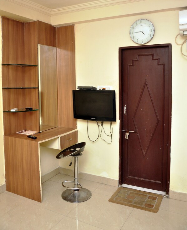A room with a wooden cabinet, a television mounted on the wall, a door, and a tiled floor.