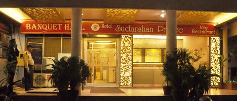 A hotel entrance with a reception desk, a Banquet Hall sign, and a Veg Restaurant sign.