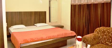 A hotel room with a bed, a sofa, a bedside table with a kettle, glasses, and a remote control.