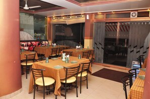 A restaurant with multiple tables and chairs, a ceiling fan, and a large window with a view of the street.