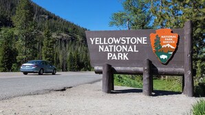 A sign for Yellowstone National Park with a car in the background. - Wilderness Pines, Close to Yellowstone, Sleeps 10 (Island Park)