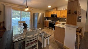 A kitchen with wooden cabinets, stainless steel appliances, a dining table with chairs, and a view of the outdoors. - Wilderness Pines, Close to Yellowstone, Sleeps 10 (Island Park)