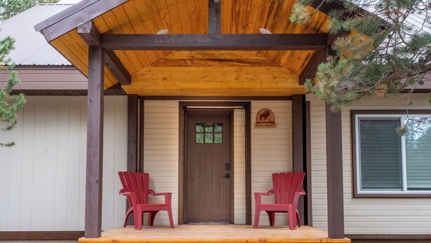A wooden porch with two red chairs, a brown door, and a window to the right. - Wilderness Pines, Close to Yellowstone, Sleeps 10 (Island Park)