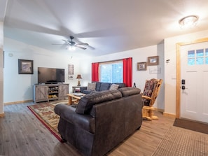 A living room with a sofa, a TV, a ceiling fan, and a wooden door.