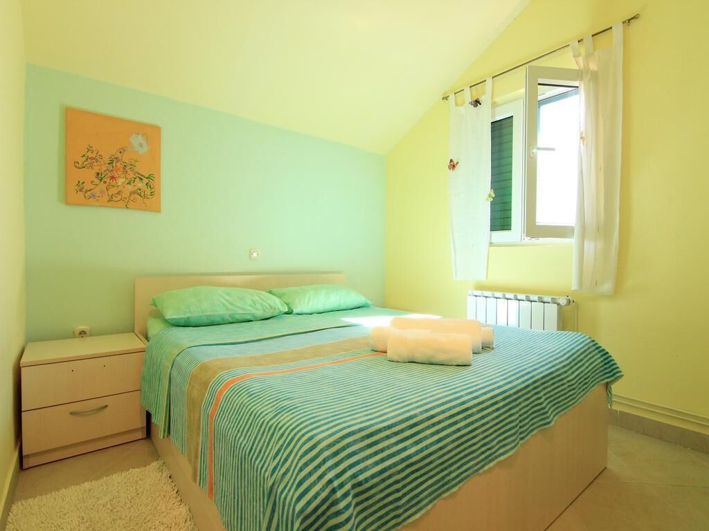 Un dormitorio con una cama, una mesita de noche, una ventana con cortinas y un cuadro en la pared.