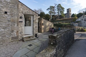 A stone building with a door, steps leading to the entrance, and a stone wall in the foreground.