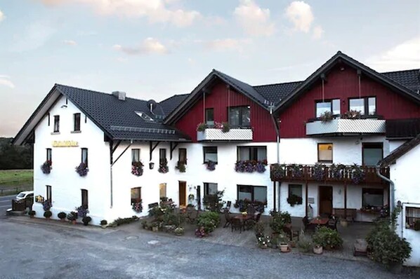 Un edificio de dos pisos con fachada blanca y detalles en rojo, que cuenta con varios balcones con macetas.