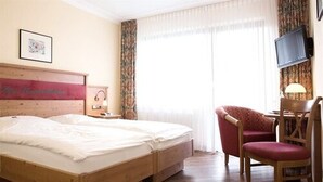 A hotel room with a double bed, a desk with a chair, a television, and a window with curtains. - Landgasthof Gut Marienbildchen (Roetgen)