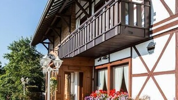 A traditional half-timbered building with a balcony, potted plants, and a barrel. - Landgasthof Gut Marienbildchen (Roetgen)