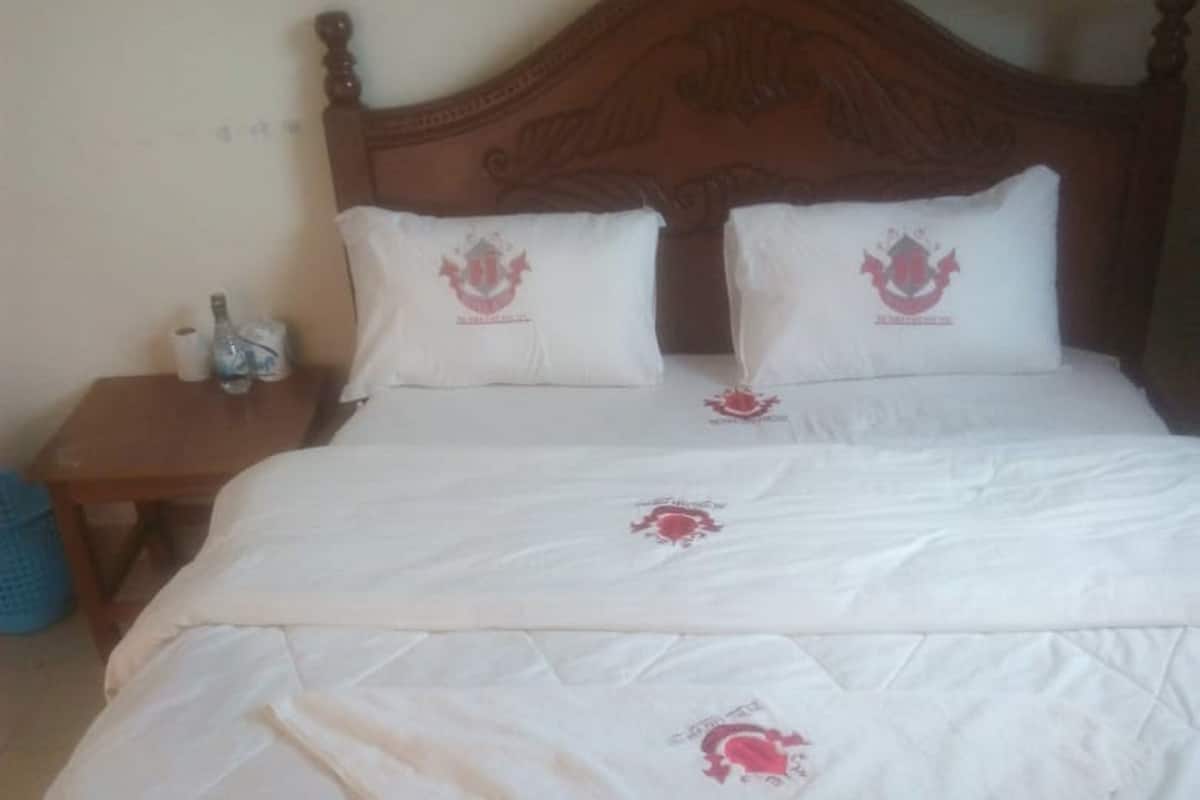 Una cama con cabecera de madera, ropa de cama blanca y almohadones decorativos con un emblema rojo.