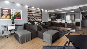 Una sala de estar moderna con un sofá seccional gris, un comedor con una mesa negra y una cocina al fondo.
