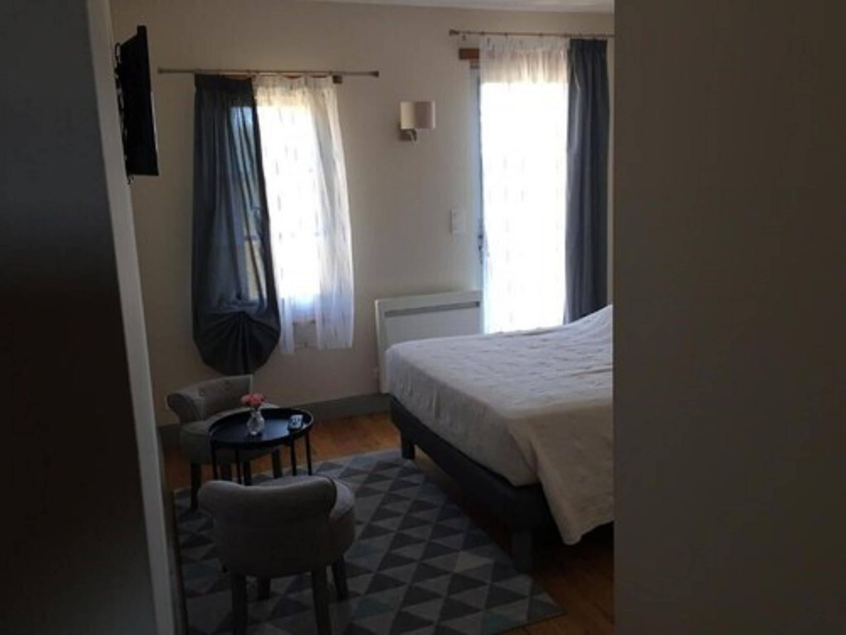 A bedroom with a bed, a chair, a small table, and a window with curtains.