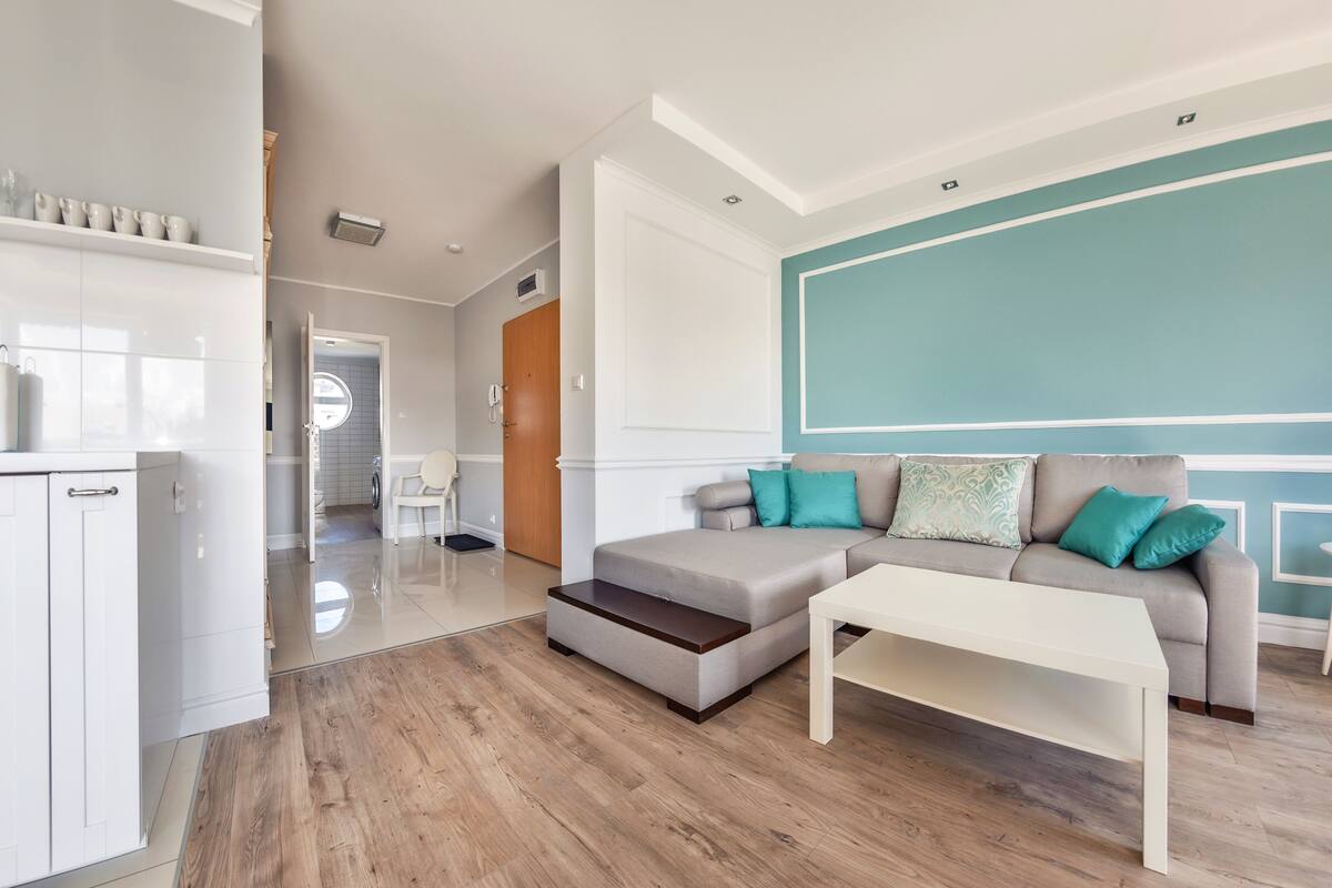 Una sala moderna con un sofá gris, cojines color turquesa y una mesa de centro blanca.