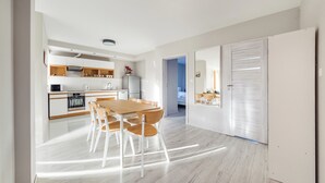 Une cuisine moderne avec des meubles blancs, une table à manger en bois et une vue sur une chambre.