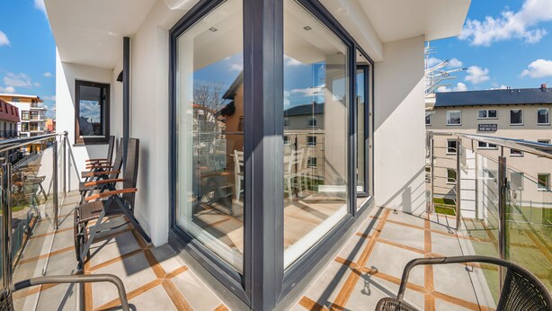 Un balcon moderne avec des portes vitrées, un espace salon extérieur et une vue sur les bâtiments voisins.