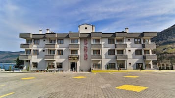 Ein mehrstöckiges Hotel mit einem Balkon an jeder Etage, einer Schrifttafel mit der Aufschrift „Sunrise Hotel“ und einer gepflasterten Fläche davor.