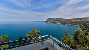 A coastal view from a balcony with a railing, overlooking a clear blue sea and a hilly landscape with buildings in the distance. - Amasra Sunrise Otel (Amasra)