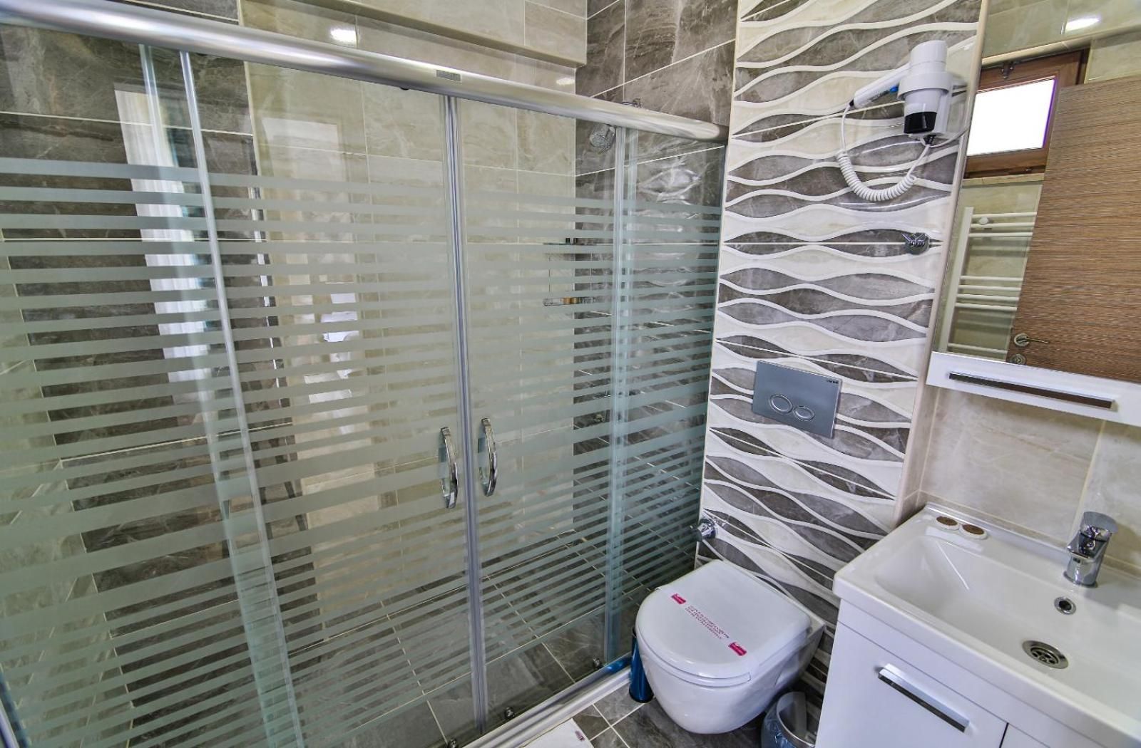 A bathroom with a glass shower enclosure, a toilet, and a sink with a mirror above it.