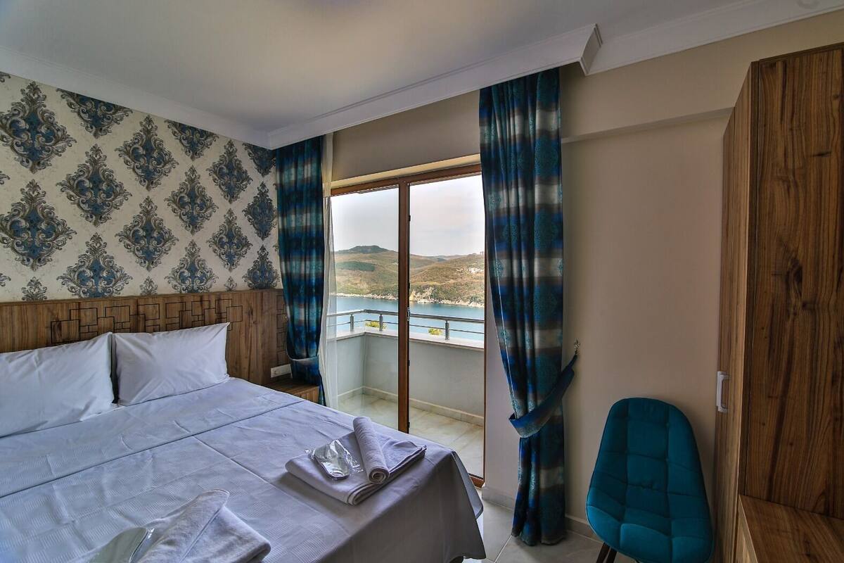 Una habitación de hotel con una cama grande, un balcón con vistas al mar y un armario de madera.