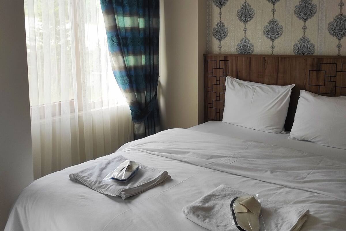Una habitación de hotel con una cama grande, cabecera con diseño geométrico y ventana con cortinas traslúcidas.