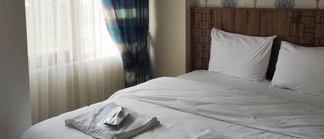 Una habitación de hotel con una cama grande, cabecera con diseño geométrico y ventana con cortinas traslúcidas.