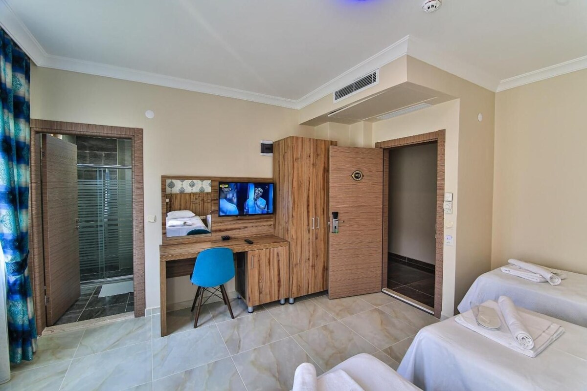 A hotel room with a bed, a desk with a computer and TV, a shower, and a wardrobe.