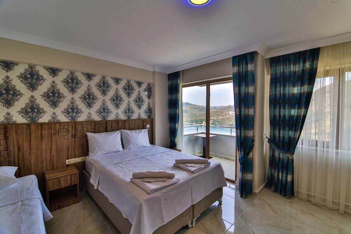 Habitación de hotel con una cama grande, cabecera de madera, mesita de noche y vista al mar desde un balcón.