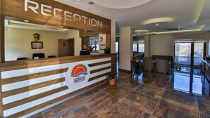 A reception area with a wooden reception desk, a logo with a sun and the word "SUNRISE," and a view of the outdoor balcony. - Amasra Sunrise Otel (Amasra)
