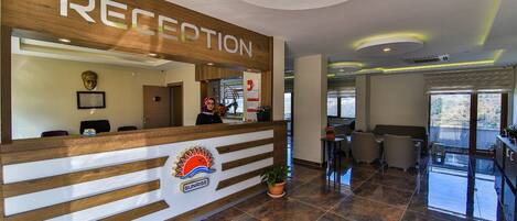 A reception area with a wooden reception desk, a logo with a sun and the word "SUNRISE," and a view of the outdoor balcony.