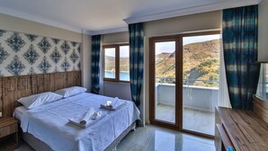 A hotel room with a bed, a wooden headboard, a balcony with a view of hills, and a television on a wooden table. - Amasra Sunrise Otel (Amasra)