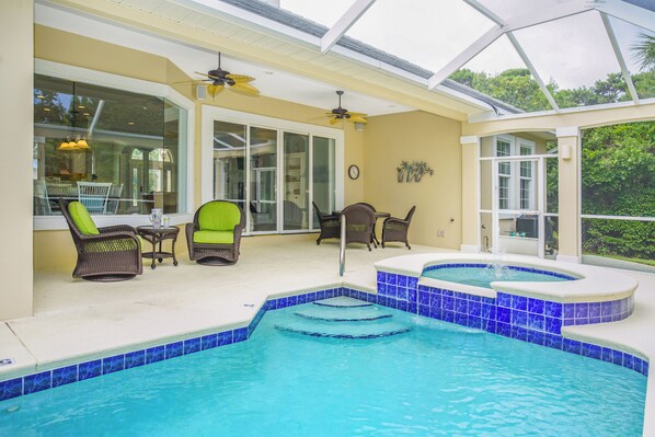 A swimming pool with blue tiles, surrounded by wicker chairs and a hot tub.