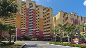 A multi-story hotel with a red and yellow facade, multiple balconies, and palm trees in the foreground. - Calypso Resort by BBG (Panama City Beach)