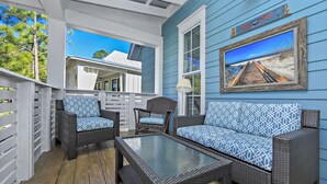 A covered outdoor seating area with wicker furniture and a glass-top table, overlooking a beach scene. - Dream Weaver - 1232968 (Santa Rosa Beach)