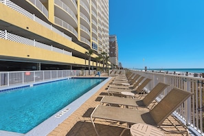 A poolside area with lounge chairs, a swimming pool, and a building with multiple balconies.