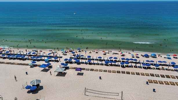 Ein Strand mit Liegestühlen und Sonnenschirmen, einem Volleyballnetz und dem Meer im Hintergrund.