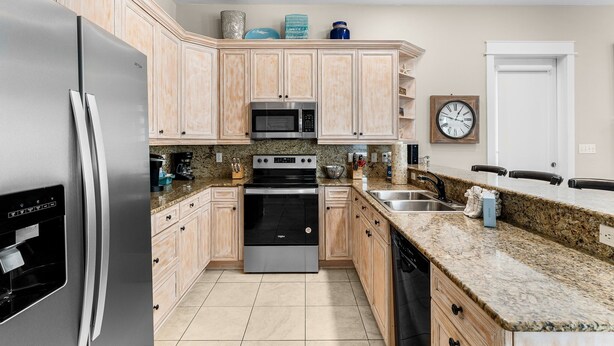 A kitchen with a stainless steel refrigerator, a microwave, an oven, granite countertops, wooden cabinets, and a clock on the wall. - Amazing Place - 1232960 (Santa Rosa Beach)