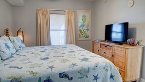 Ein Schlafzimmer mit einem Bett, einer Holzkommode, einem Fernseher und einem Gemälde von einem Seepferdchen an der Wand.
