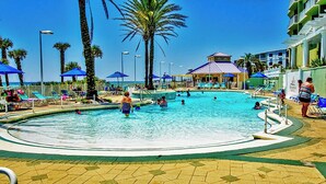 Un espace piscine doté de plusieurs couloirs, de palmiers et de parasols de plage.