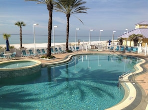 Une piscine aux eaux cristallines, bordée de chaises longues et de palmiers, entourée d’une clôture et offrant une vue sur la plage.